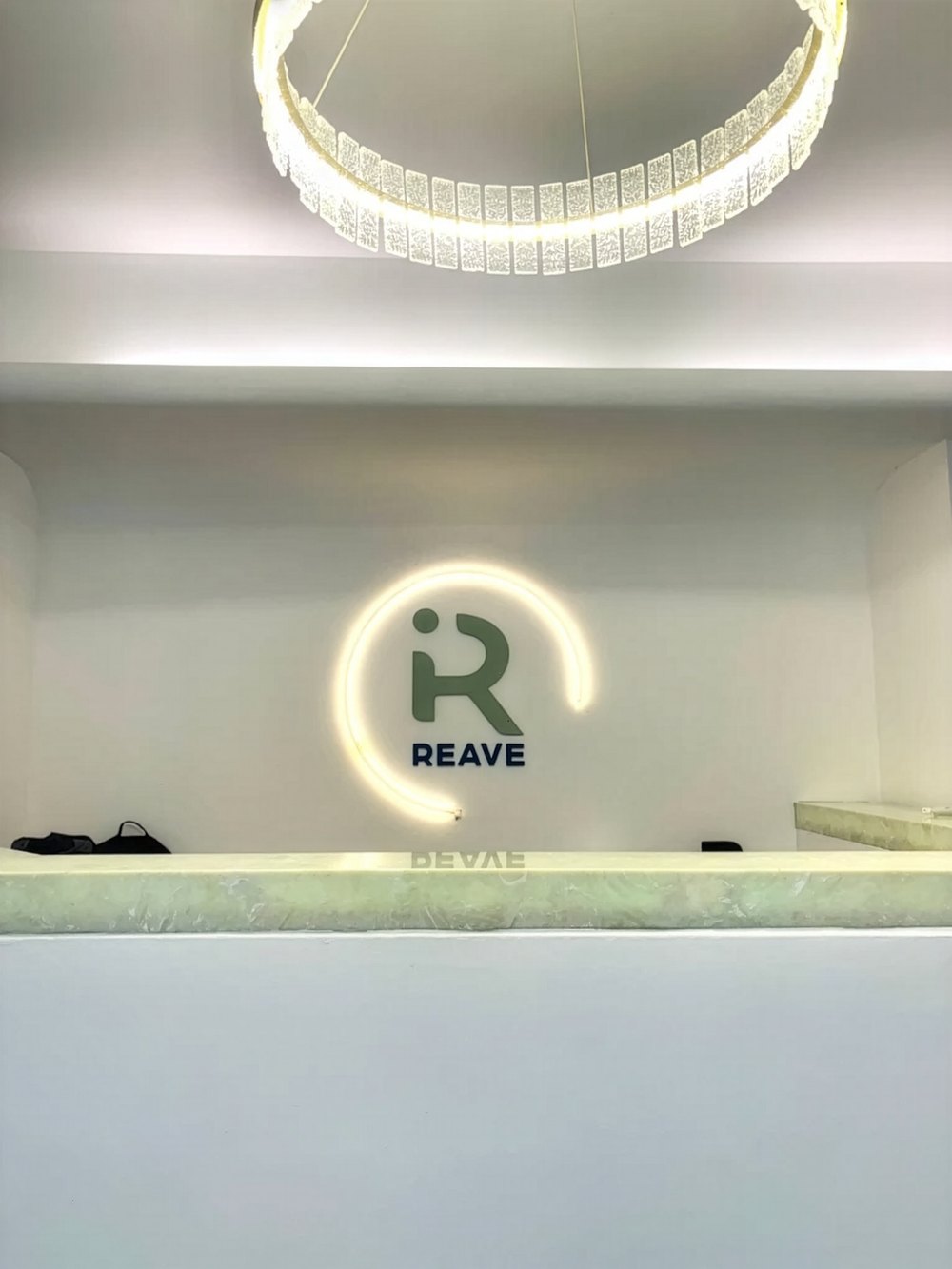 Recepção da Clínica Reave em Itapema, com o logotipo iluminado na parede e o balcão de atendimento