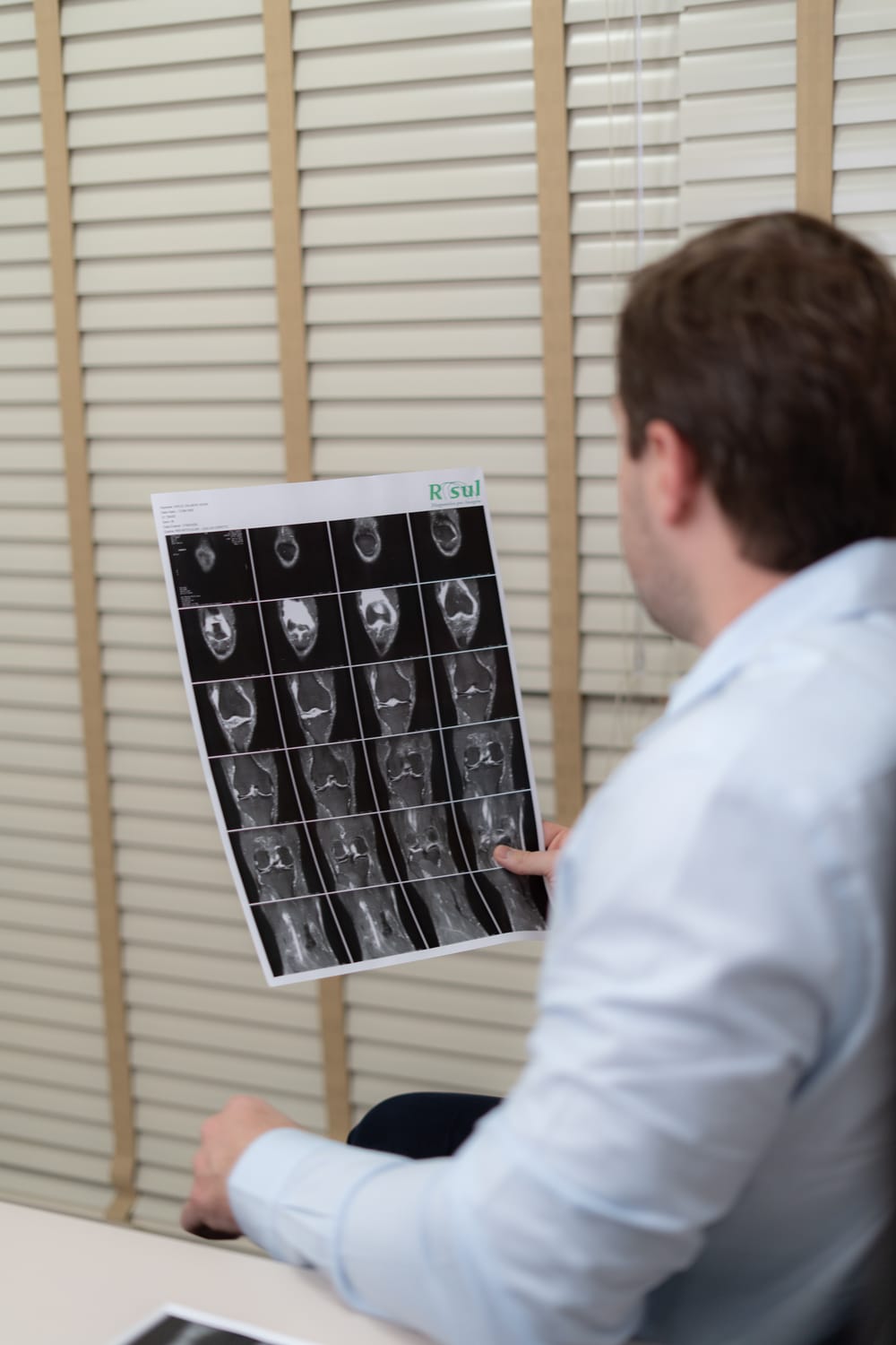 Dr. Fernando Hehn examina as imagens de uma ressonância magnética do joelho, sentado à mesa do consultório