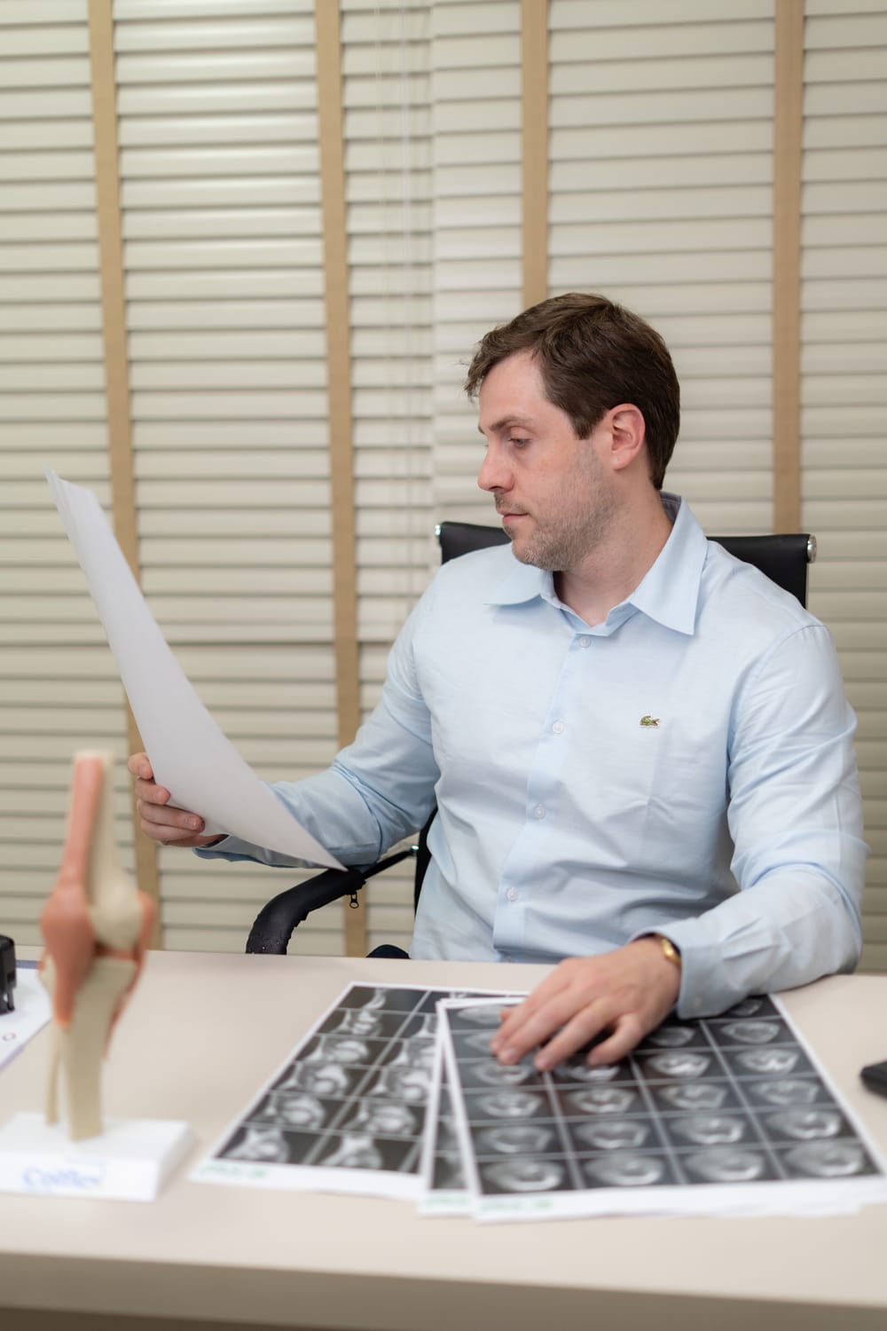 Dr. Fernando Hehn analisa exames de ressonância magnética do joelho no consultório, com um modelo anatômico sobre a mesa
